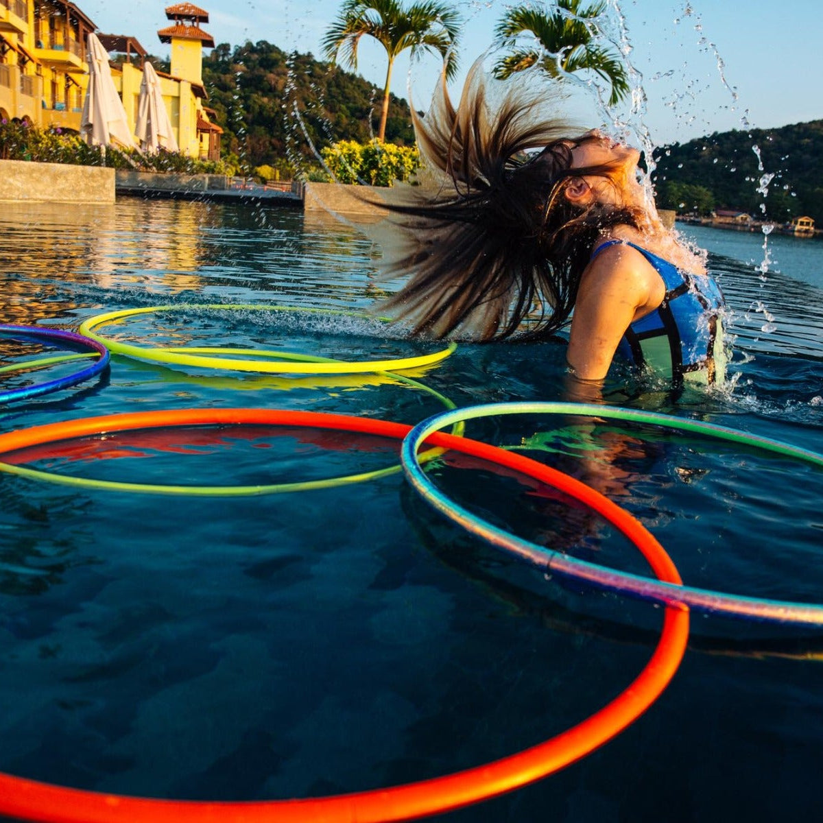 Person playing with colorful hula hoops in a pool with a scenic background